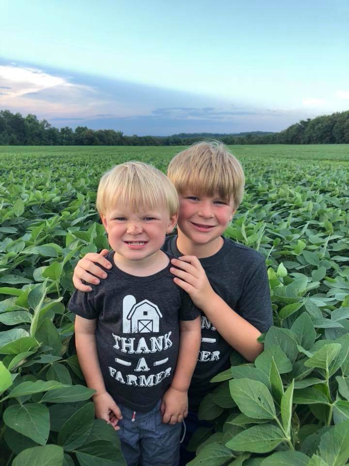 Two young brother smiling and embracing in a field of lush, green crops